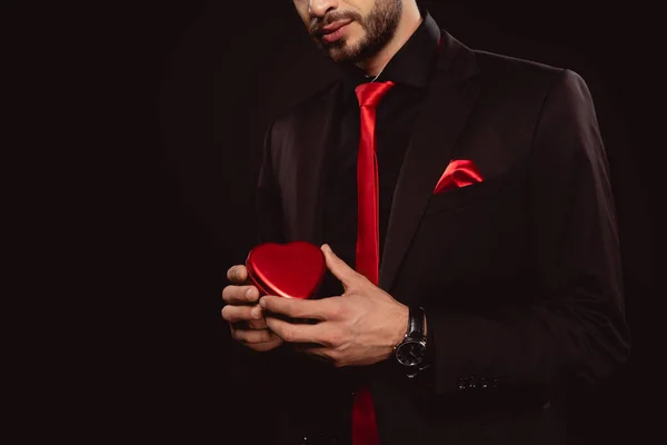 Cropped view of elegant man holding heart shaped gift box isolated on black — Stock Photo