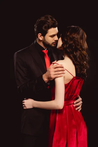 Hombre guapo en traje quitando vestido rojo de novia hermosa aislado en negro - foto de stock