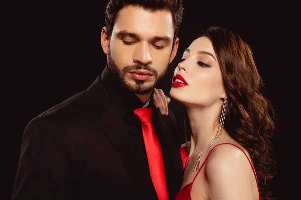 Elegant woman looking at handsome boyfriend in suit and red tie isolated on black — Stock Photo