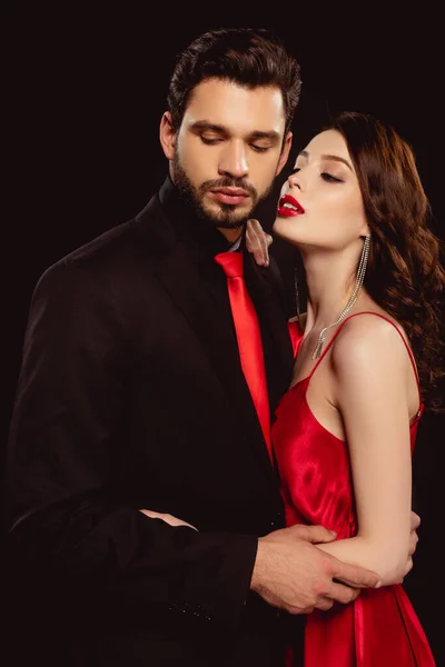 Belle jeune femme en robe embrassant beau petit ami isolé sur noir — Photo de stock