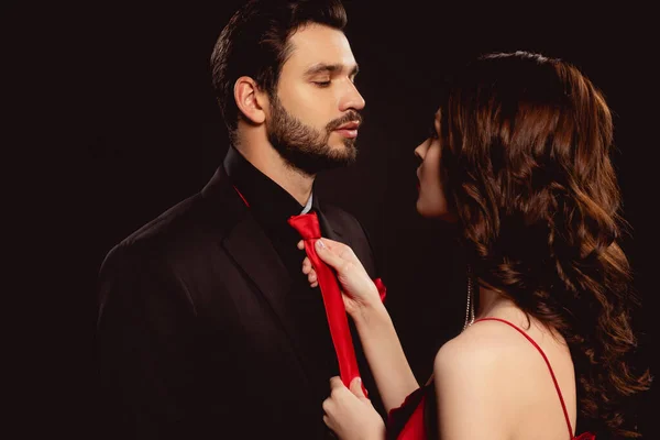 Beautiful woman adjusting tie of handsome boyfriend isolated on black — Stock Photo