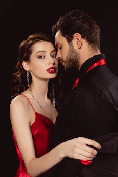 Side view of elegant girl with red lips taking off jacket of boyfriend and looking at camera isolated on black — Stock Photo