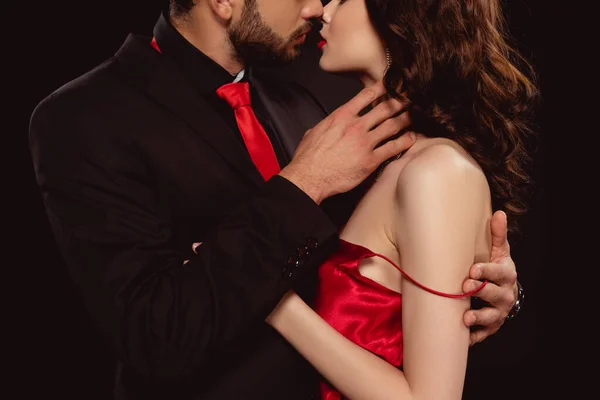 Vista recortada de hombre elegante besándose y quitándose vestido rojo de novia aislado en negro - foto de stock