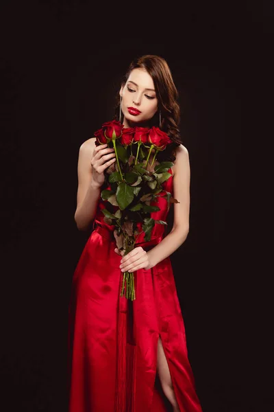 Mulher elegante em vestido vermelho segurando rosas isoladas em preto — Fotografia de Stock