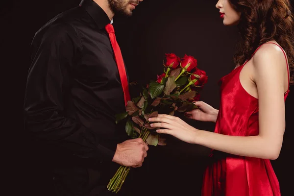 Vista recortada del hombre dando ramo de rosas a la mujer elegante aislado en negro - foto de stock