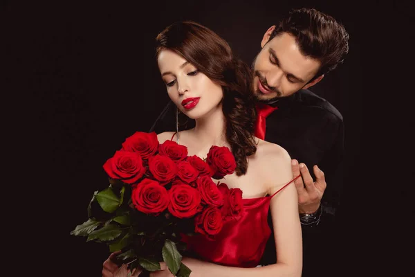 Elegante hombre quitándose el vestido de novia con rosas rojas aisladas en negro - foto de stock