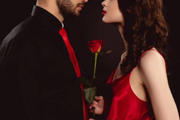 Vue recadrée de femme élégante tenant rose près du petit ami isolé sur noir — Photo de stock