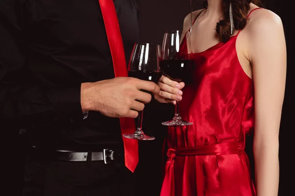 Vista recortada de pareja elegante tintineo con vino tinto aislado en negro - foto de stock