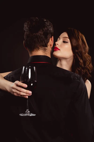Beautiful woman with glass of wine embracing boyfriend isolated on black — Stock Photo
