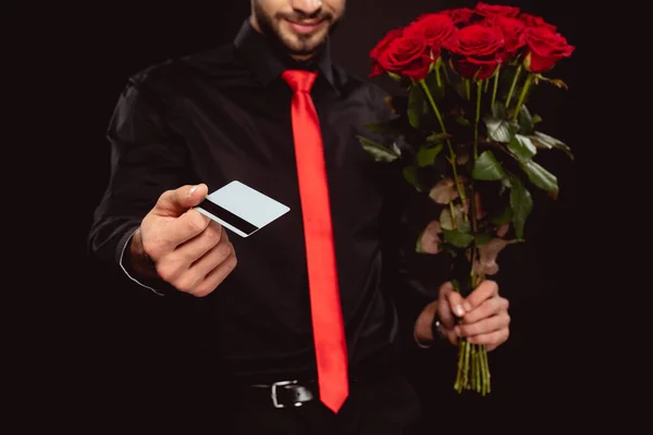 Ausgeschnittene Ansicht eines eleganten Mannes mit Kreditkarte und Rosen, während er die Kamera isoliert auf schwarz betrachtet — Stockfoto