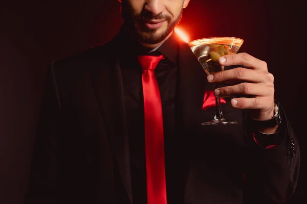 Cropped view of elegant man holding glass of cocktail on black background with lighting — Stock Photo