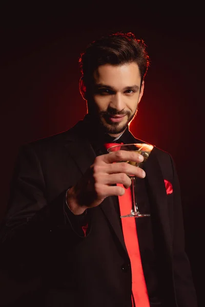 Красивий чоловік у костюмі тримає склянку коктейлю на чорному тлі з освітленням — стокове фото