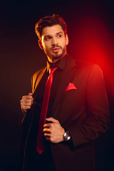 Handsome man looking away while adjusting jacket on black background with lighting — Stock Photo