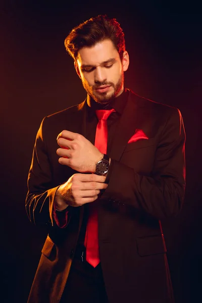 Elegant man in suit adjusting wristwatch isolated on black — Stock Photo