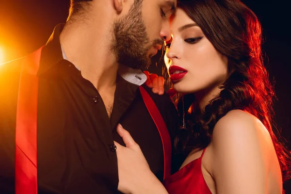 Sensual woman touching chest of handsome boyfriend with unbuttoning shirt on black background with lighting — Stock Photo