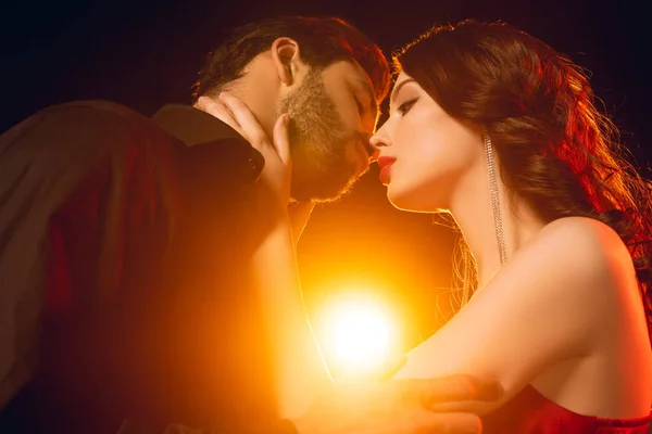 Niedriger Winkel Ansicht der eleganten Frau küsst schönen Freund auf schwarzem Hintergrund mit Beleuchtung — Stockfoto