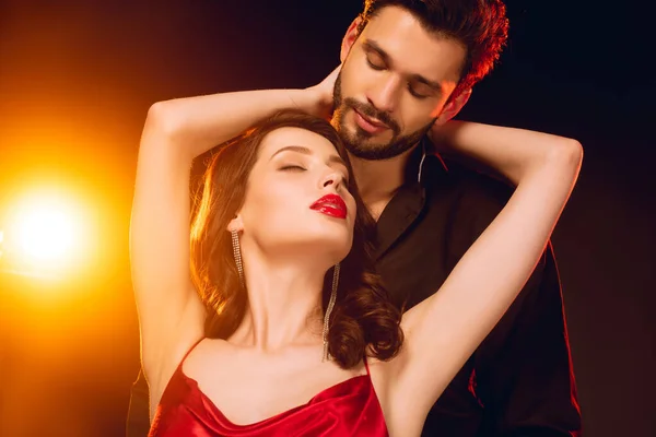 Elegant girl embracing handsome boyfriend on black background with lighting — Stock Photo