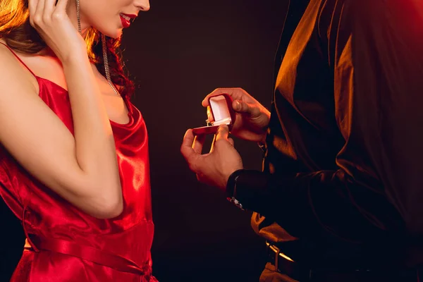 Cropped view of man giving box with jewelry ring to elegant girlfriend isolated on black — Stock Photo