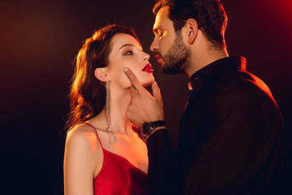 Side view of handsome man kissing and touching face of beautiful girl isolated on black — Stock Photo