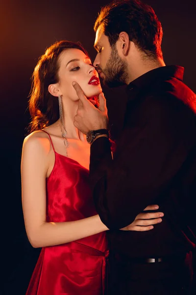 Handsome man kissing elegant girlfriend with red lips isolated on black — Stock Photo