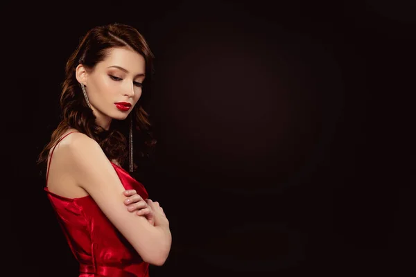 Vista lateral de hermosa mujer en vestido rojo con brazos de cruces aislados en negro - foto de stock
