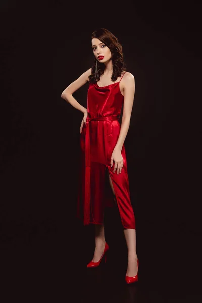 Comprimento total da mulher bonita em vestido vermelho olhando para a câmera isolada no preto — Fotografia de Stock