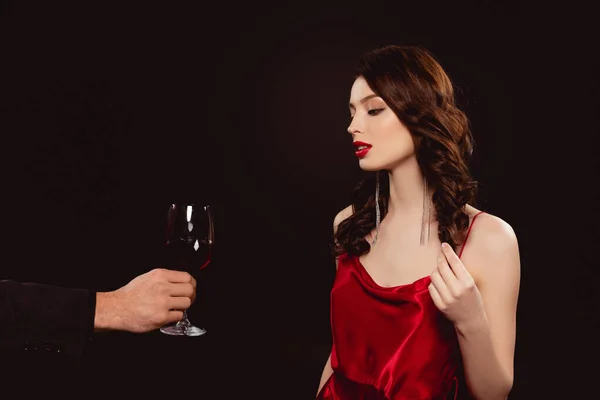 Hombre dando copa de vino tinto a mujer elegante en vestido aislado en negro - foto de stock