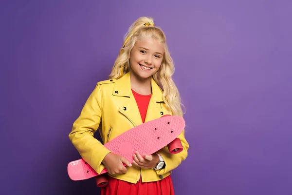 Smiling and cute kid holding penny board on purple background — Stock Photo