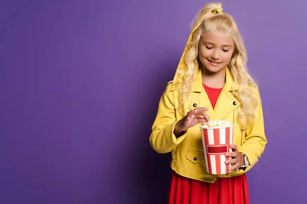 Lächelndes Kind mit Eimer mit Popcorn auf lila Hintergrund — Stockfoto