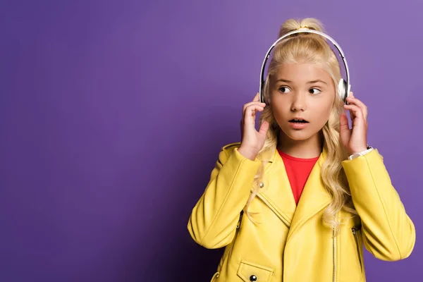 Chaval con auriculares mirando hacia otro lado sobre fondo púrpura - foto de stock