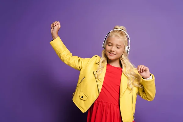 Lächelndes Kind mit Kopfhörern, Musik hörend und auf violettem Hintergrund tanzend — Stockfoto