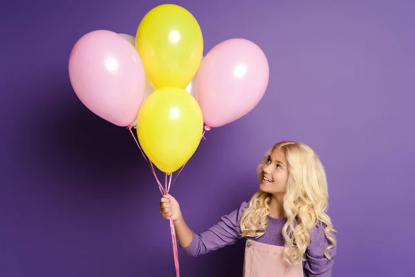 Bambino sorridente che tiene e guarda palloncini su sfondo viola — Foto stock