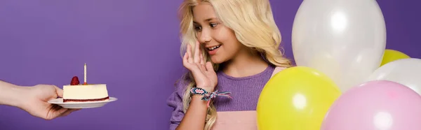 Plan panoramique de femme donnant assiette avec gâteau d'anniversaire à enfant souriant avec ballons sur fond violet — Photo de stock