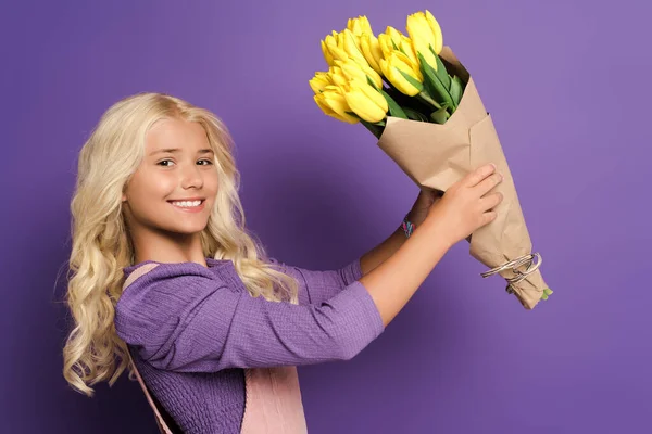 Bambino sorridente che tiene bouquet di tulipani su sfondo viola — Foto stock