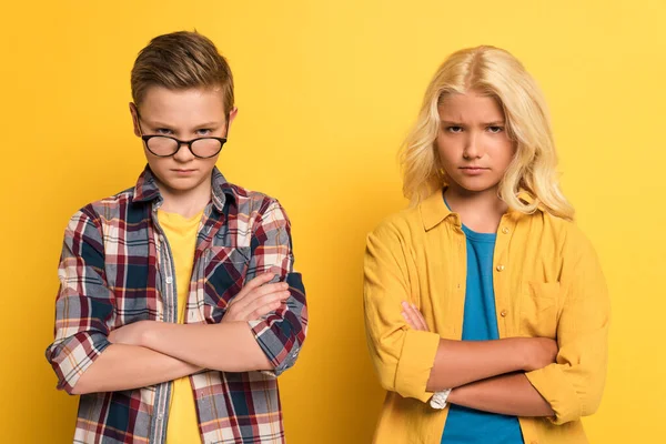 Offended kids with crossed arms looking at camera on yellow background — Stock Photo