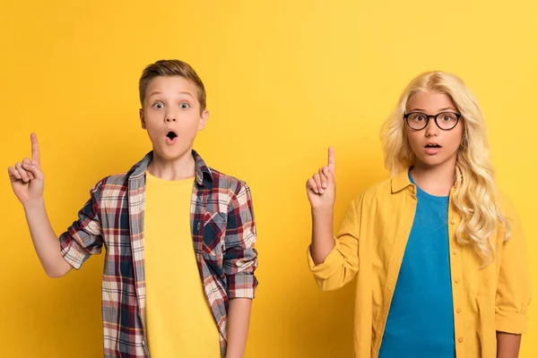 Шоковані і милі діти, що показують жест ідеї на жовтому тлі — стокове фото