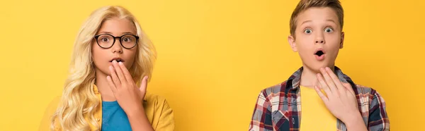 Panoramic shot of shocked kids looking at camera on yellow background — Stock Photo