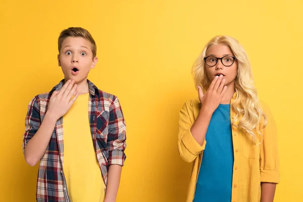 Shocked and cute kids looking at camera on yellow background — Stock Photo