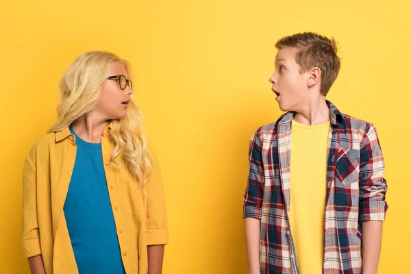 Shocked kids looking each at other on yellow background — Stock Photo