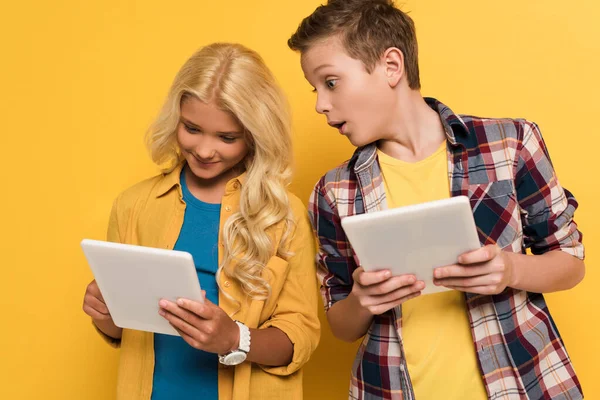 Chaval sorprendido mirando tableta digital de su amigo sonriente sobre fondo amarillo - foto de stock