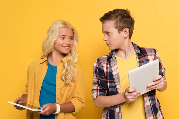 Garoto sorrindo olhando para tablet digital de sua amiga no fundo amarelo — Fotografia de Stock