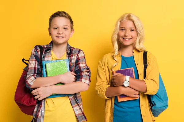 Lächelnde Schulkinder mit Büchern, die auf gelbem Hintergrund in die Kamera schauen — Stockfoto