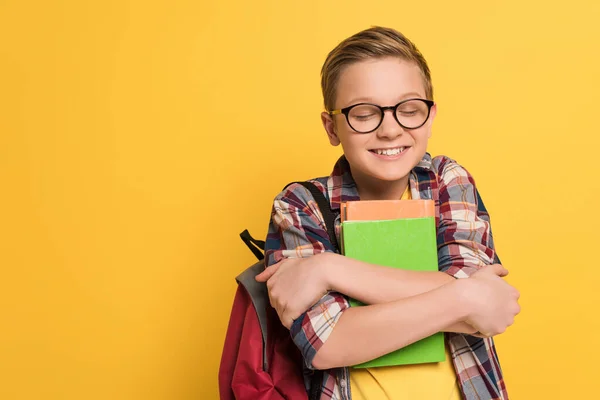 Lächelnder Schuljunge mit geschlossenen Augen, Bücher isoliert auf gelb haltend — Stockfoto