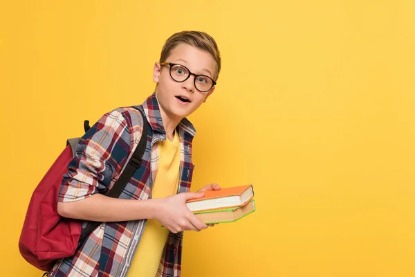 Shocked schoolboy with glasses holding books isolated on yellow — Stock Photo