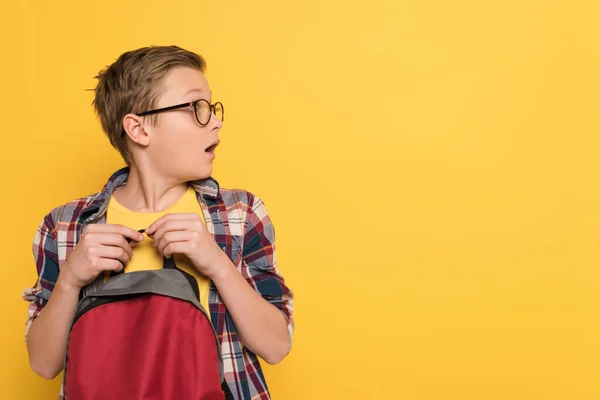 Scioccato scolaro con occhiali tenendo zaino isolato su giallo — Foto stock