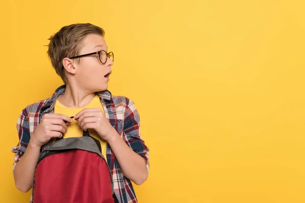 Schockierter Schüler mit Brille hält Rucksack isoliert auf gelb — Stockfoto