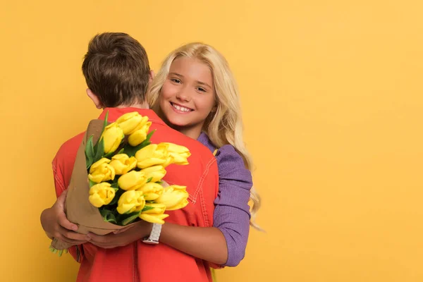 Back view of boy hugging smiling friend with bouquet on yellow background — Stock Photo