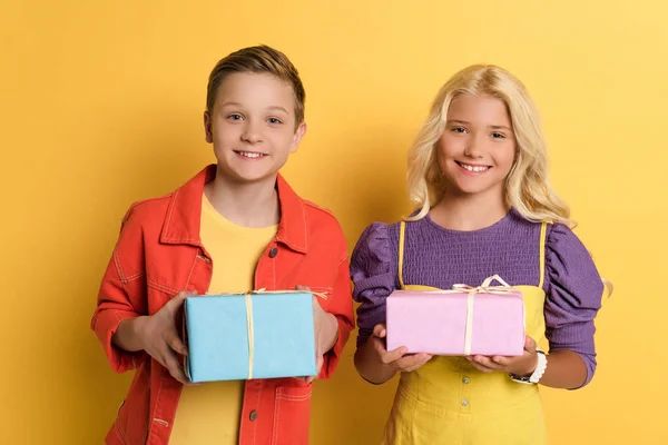 Amigos sonrientes sosteniendo cajas de regalo sobre fondo amarillo - foto de stock