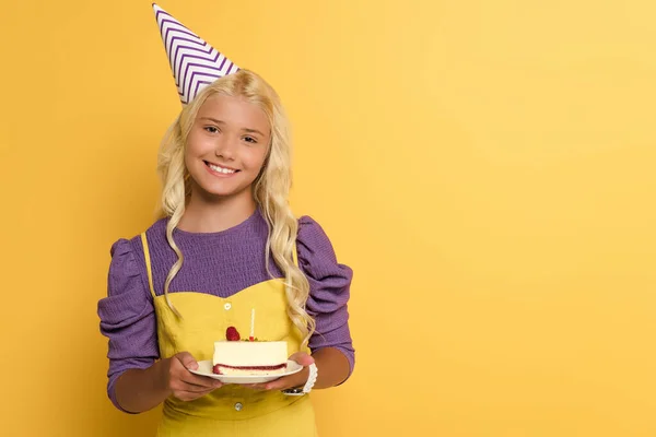 Niño sonriente sosteniendo plato con pastel de cumpleaños sobre fondo amarillo - foto de stock