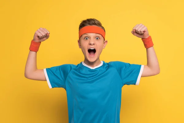 Niño enojado en ropa deportiva mostrando un gesto fuerte y gritando sobre el fondo amarillo - foto de stock